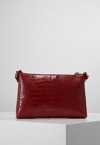 Rød håndtaske med krokodilleprægning og en glat, skinnende finish. Har en aftagelig rem og en rektangulær form, velegnet til afslappet brug.
