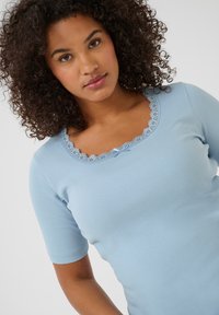 Light blue ribbed short-sleeve top with a scalloped lace neckline featuring a bow detail. Made from soft, stretchy fabric.