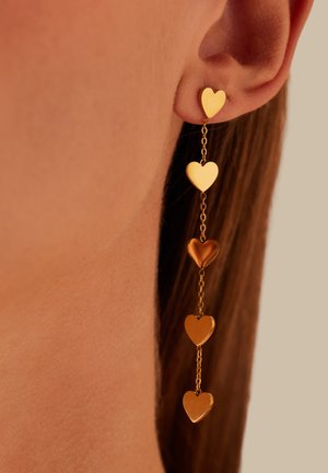 Ear with gold dangling earring featuring five connected heart-shaped charms in varying metallic shades.