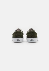 Zapatillas de ante verde con un perfil bajo, suela de goma blanca, etiqueta de logo distintiva en la parte trasera y acentos texturizados en el talón.