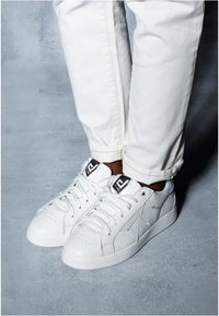 Białe skórzane sneakersy o fakturowanym wykończeniu, z gwiazdą na boku, białymi sznurowadłami i czarnymi akcentami logo na języku.