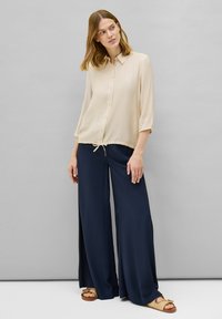 Crème overhemd met knopen en driekwartmouwen; gecombineerd met marineblauwe wijde broek. Sandalen hebben een geweven ontwerp. Eenvoudige, ontspannen pasvorm.