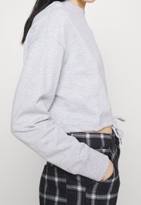 Sudadera gris corta con mangas largas y cordón en el dobladillo, combinada con pantalones a cuadros en blanco y negro con bolsillos laterales.
