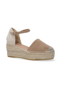 Beige ruskinds wedge espadrille med justerbar ankelstrop, vævet sidesektion og lukket tå, som har en jute reb sål og tekstureret tåhætte.