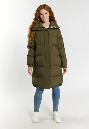 Olijfgroen pufferjack met een hoge kraag, voorritssluiting en gestikte details. Beschikt over een gebogen zoom en zijzakken. Gecombineerd met blauwe jeans en witte sneakers.