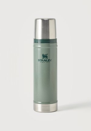 Termo Stanley verde con tapa y base plateadas, de pie sobre un fondo liso.