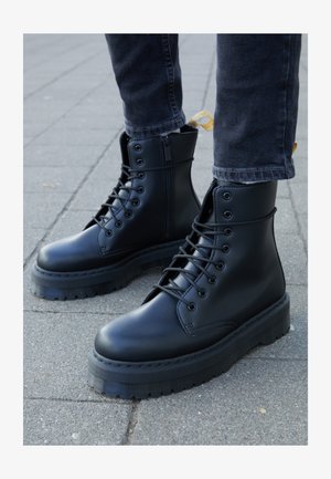 Schwarze Lederkampfstiefel mit einer dicken, geriffelten Sohle, Schnürverschluss an der Vorderseite und einem Reißverschluss an der Seite, ausgestattet mit einer abgesetzten Zuglasche.