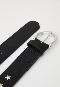 Bracelet de montre en cuir noir avec une boucle en argent, présentant des embellissements en forme d'étoile et des détails de couture le long de sa longueur.