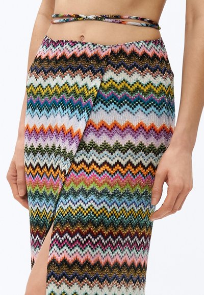 Srednji del telesa in spodnji trup osebe, ki nosi večbarvno krilo s cikcak vzorcem in stranskim razporkom ter ujemajoče se vrvice vrhnjega dela, ki se ovije okrog telesa.