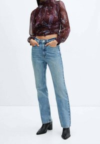 Jean droit bleu taille haute avec poches avant, associé à un top transparent à motif paisley maroon et des bottines à talons noires.