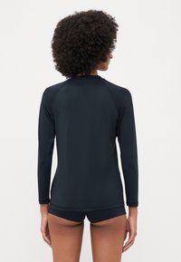Melns garās piedurknes rash guard, izgatavots no elastīgas, mitrumu uzsūcošas auduma, ar raglānu piedurknēm un pieguļošu dizainu.