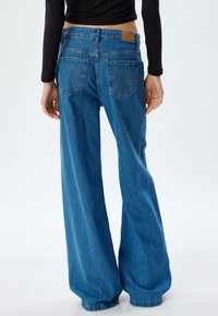 Breda ben blå denimjeans med hög midja, med en läderlapp på baksidan, två bakfickor och en blekt textur.