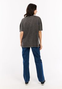 Heren t-shirt in houtskoolkleur, oversized met verlaagde schouders, afgewerkte randen en een relaxed fit, gecombineerd met lichtblauwe rechte jeans en zwarte sneakers.