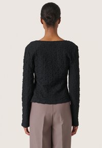 Maglione nero con texture, colletto rotondo e maniche lunghe, caratterizzato da un design in tessuto stropicciato. Abbinato a pantaloni marrone chiaro.