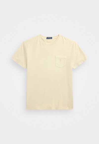 T-shirt de manga curta na cor creme, feito de algodão, com um bolsinho no peito e um clássico decote redondo. Textura suave, design simples.
