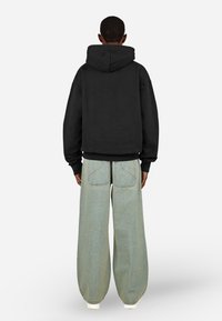 Čierna mikina s kapucňou a voľným strihom, kombinovaná so svetlo modrými širokými džínsami s vreckami na zadnej strane a textúrovaným prevedením.