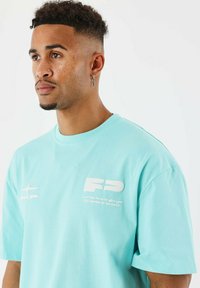 Camiseta de algodón azul claro con un corte holgado, que presenta texto gráfico blanco y un logo en la parte frontal, cuello redondo y mangas cortas.