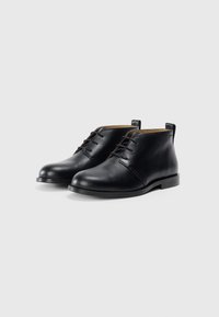 Botine din piele neagră, cu vârf rotund, cu șireturi în față și finisaj neted. Au un toc jos și elemente de design minimalist.