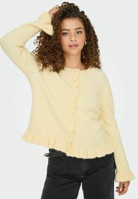 Cardigan en maille jaune avec des accents côtelés, ouverture à boutons, et ourlet et bords de manches froncés. Texture douce, coupe décontractée.