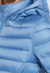 Niebieska kurtka puchowa z błyszczącym wykończeniem, posiadająca zamek błyskawiczny z przodu, kaptur oraz przeszycia w formie pikowanych wzorów zapewniających izolację.