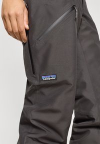 Μαύρο παντελόνι ανθεκτικό στο νερό με τσέπες με φερμουάρ, φέρει λογότυπο Patagonia. Το ύφασμα έχει λείο, ανθεκτικό υφή.