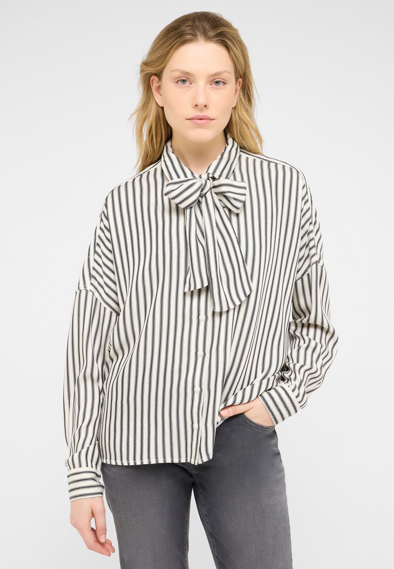 Striped blouse in cream and black, featuring a bow tie collar, buttoned front, and relaxed fit sleeves. Soft, lightweight material.