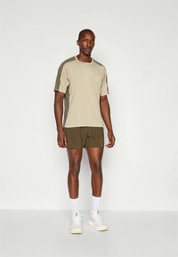 Camisa de manga corta color caqui con detalles en verde oliva, combinada con pantalones cortos en verde oliva. Tejido suave, ajuste relajado y zapatillas deportivas blancas con detalles.