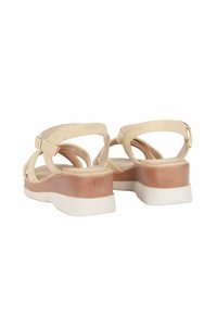 Sandali beige con cinturini incrociati e soletta imbottita. Presentano un tacco a blocco in tonalità legno chiaro con una suola in gomma bianca.