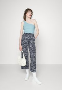 Top assimétrico azul claro, calças largas com padrão em azul marinho e estampado floral branco, acessórios brancos incluindo uma mala e ténis.