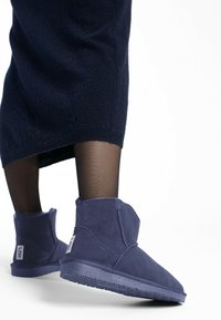 Botines cortos azul marino de ante con una textura suave, con puntera redonda y suela de goma texturizada. Con un remache en la parte trasera.