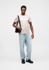 Φωτεινή μπεζ μπλούζα με διακριτικό σχέδιο, άνετο ανοιχτό μπλε τζιν, μαύρη τσάντα ώμου με λουρί και μαύρα παπούτσια.