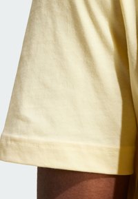 Pantalones cortos de algodón amarillo claro con una textura suave, bordes dobladillados y un ajuste relajado, mostrando parcialmente un tono de piel más oscuro en el dobladillo.