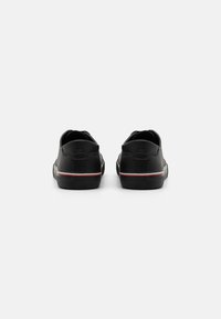 Mustad mustad madalad sneakersid, millel on punane ja valge triip põhjaga, vaadatuna tagant, valge tausta ees.
