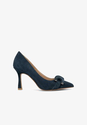 Pump in suede blu navy con tacco alto e punta affilata, caratterizzato da un accento decorativo a nodo e un tacco slanciato. Fodera interna liscia.