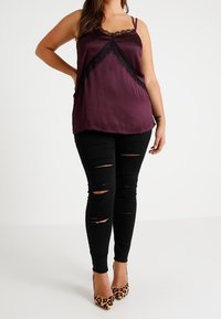 Kvinna iklädd en ärmlös lila satin topp med svart spetsdetalj, svarta rivna skinny jeans och högklackade leopardmönstrade skor.