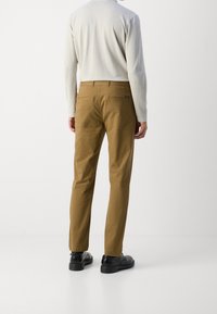 Beige katoenen broeken met een rechte snit, twee achterzakken en een riemlus. Gecombineerd met zwarte schoenen en een lichtgekleurde lange mouw top.