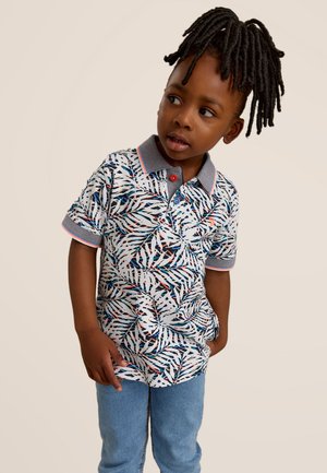 Polo-shirt à manches courtes avec un motif de feuilles colorées, col gris, accents rouges et patte de boutonnage à deux boutons, associé à un jean bleu clair.