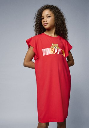 Punainen puuvillahame, jossa on kelluvat hihat ja karhukuva, sekä sana "MOSCHINO" lihavilla keltaisilla ja vaaleanpunaisilla kirjaimilla rinnan kohdalla.