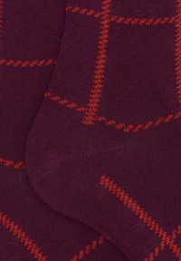Primo piano di calzini di maglia viola con un motivo a zigzag rosso a quadretti nelle sezioni del tallone e del piede.