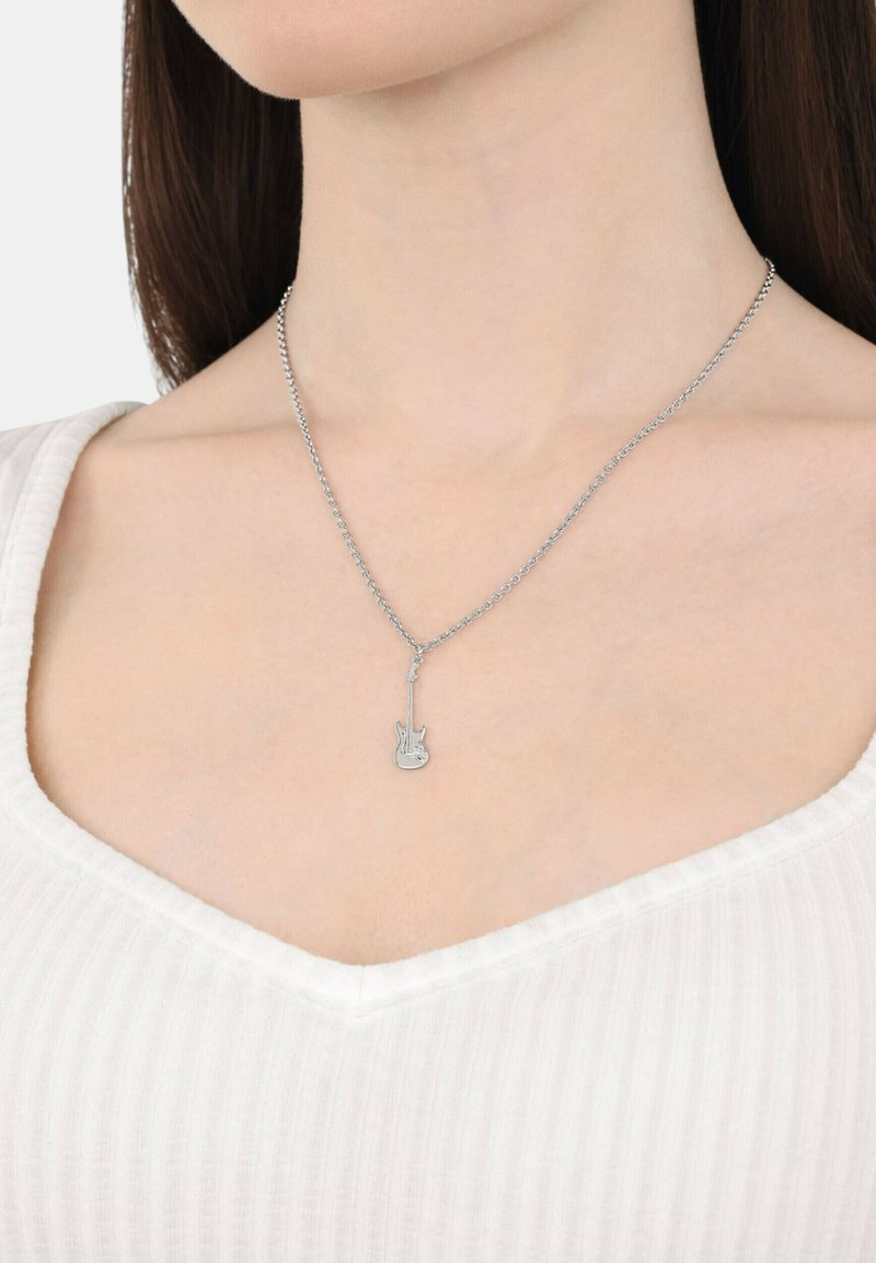 Collana con pendant a forma di chitarra in argento, su una catena sottile, caratterizzata da una forma di chitarra dettagliata, indossata su un top a scollatura a V con una texture a coste.