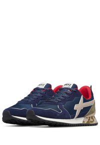 Scarpe sportive blu con una combinazione di suede e nylon, dettagli rossi e un tallone beige con motivo camo. Presentano una suola nera robusta e un design con lacci.