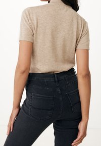 Beige short-sleeve knit top with a high collar, paired with dark gray high-waisted jeans featuring patch pockets and a smooth texture.