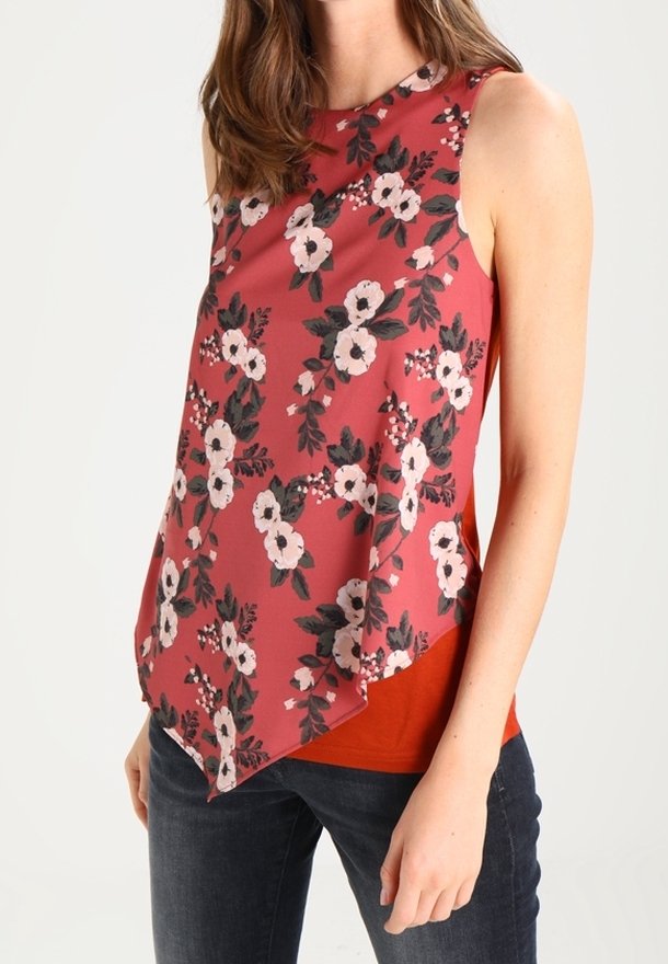Top floreale color corallo con orlo asimmetrico, decorato con fiori rosa e neri. Abbinato a jeans scuri, per un look casual.