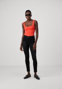 Felle oranje bodysuit met vierkante halslijn, gecombineerd met zwarte slim-fit jeans. Zwarte platte schoenen maken de look af en benadrukken een moderne, minimalistische stijl.