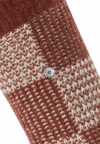 Stricksocken in Braun und Creme mit einem strukturierten Muster. Ein silberner Hardware-Akzent zeigt den Markennamen. Gemütliches und weiches Material.