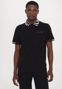 Black polo shirt with a zebra-patterned collar and contrasting embroidered branding on sleeves. Short sleeves and classic fit.