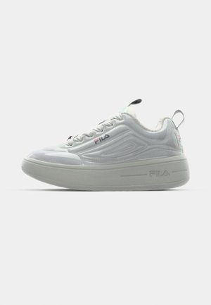 Hvide sneakers med en glansfuld finish, der har mesh-detaljer, en tyk grå sål og snørebånd foran. Fila-logoet er vist på siden.