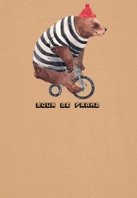 Een beer rijdt op een kleine blauwe fiets, draagt een zwart-wit gestreept shirt en een rode muts, met de tekst "TOUR DE FRANZ" eronder.
