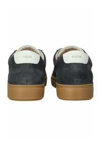 Zapatillas de ante en gris oscuro con suelas de goma marrón. Presentan acentos blancos en el talón y un logo dorado en la parte posterior. Forro interior suave.