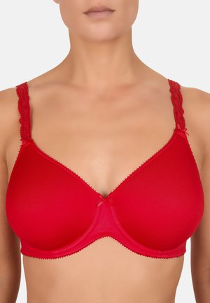 Kobieta w jaskrawoczerwonym biustonoszu z fiszbinami, z koronkowymi ramiączkami i małymi kokardkami przy ramiączkach oraz na środku z przodu.